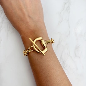 May include: A gold chain bracelet with a large, chunky, gold toggle clasp.