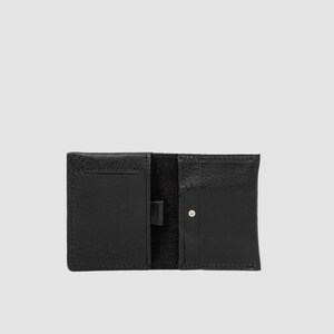 May include: A black leather wallet featuring a bi-fold design with multiple interior card slots and a central vertical strap. The exterior surface displays a textured grain, and a small silver-toned metal stud is visible on the right-hand side.