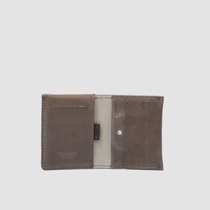 May include: A dark gray leather wallet in an open, flat orientation. The wallet features multiple card slots, visible stitching along the edges, and the embossed text GEOMETRIC GOODS on the lower left panel. The interior lining is a lighter gray.