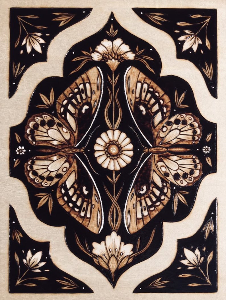 May include: A woodburned design of two butterflies mirroring each other , with a large daisy in the center. The butterflies are brown and black, and the daisy is white. The background is black with white flowers and leaves. art nouveau inspired with dark feminine traits. burned into birch wood and white charcoal highlights