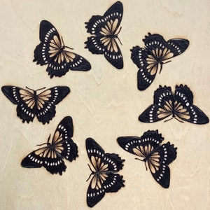 May include: Seven black and gold butterfly silhouettes on a light beige background.