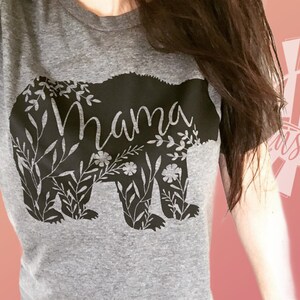 May include: Gray t-shirt with a black bear silhouette design. The bear is surrounded by floral details and the word "Mama" is written inside the bear.