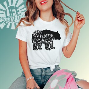 May include: White t-shirt with a black silhouette of a bear with floral details and the word "Mama" inside the bear.