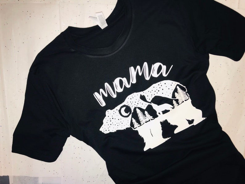May include: Black t-shirt with a white graphic of a mama bear and two cubs with mountains and the word "mama" above them.