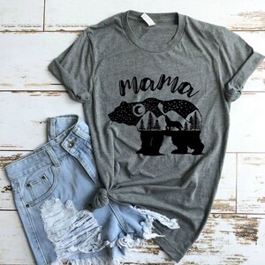 May include: Gray t-shirt with a black silhouette of a bear with a moon, stars, trees, and a wolf inside the bear. The text "mama" is above the bear.