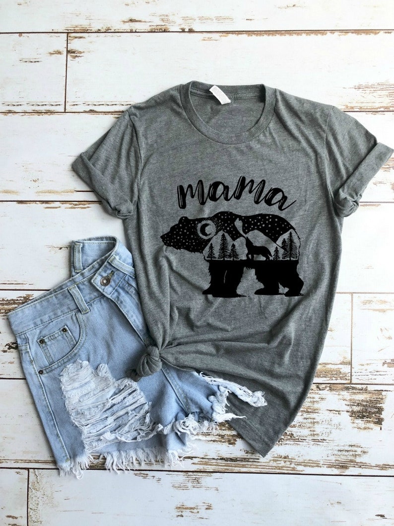 May include: Gray t-shirt with a black silhouette of a bear with a moon, stars, trees, and a wolf inside the bear. The text "mama" is above the bear.