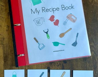 May include: A red binder labeled "My Recipe Book" with illustrated kitchen tools. Below are cards labeled "apron", "spatula", "wooden spoon", and "quarter cup". The binder and cards are on a wooden surface.