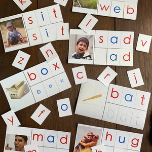 May include: A set of white cards with black and blue letters, arranged in rows to spell out words like 'web', 'sad', 'box', 'bat', 'mad', and 'hug'. The cards are on a wooden surface.