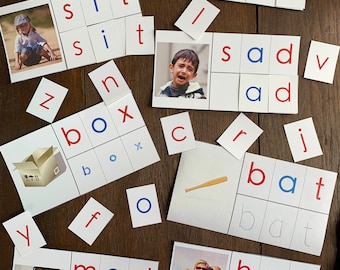 May include: A set of white cards with black and blue letters, arranged in rows to spell out words like 'web', 'sad', 'box', 'bat', 'mad', and 'hug'. The cards are on a wooden surface.