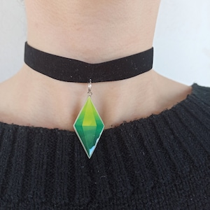 Puede incluir: Un collar gargantilla de terciopelo negro con un colgante de diamante verde y amarillo. El colgante es una representación estilizada del símbolo icónico del videojuego.