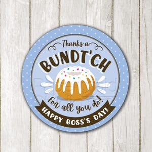 Op de afbeelding: Een ronde sticker met een lichtblauwe achtergrond en witte stippen. De sticker toont een afbeelding van een tulbandcake met hagelslag en de tekst "Thanks a Bundt'ch for all you do! Happy Boss's Day!" De tekst "Digital Download" is ook aanwezig.