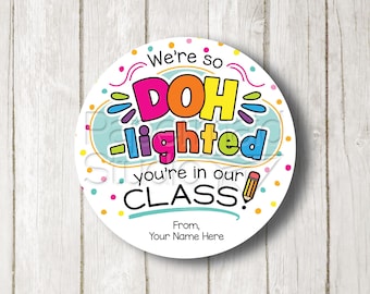 May include: A round sticker with a white background and colorful polka dots. The text reads "We're so DOH-lighted you're in our CLASS!" with a pencil icon. The text "From, Your Name Here" is at the bottom of the sticker.