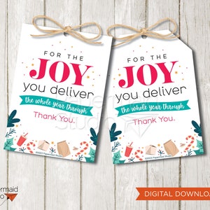 Puede incluir: Dos etiquetas de regalo blancas con un lazo de cuerda de yute. Las etiquetas dicen "FOR THE JOY you deliver the whole year through Thank You." con acentos rojos, turquesa y dorados. El borde inferior tiene ilustraciones festivas.