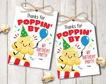 May include: Two white favor tags with a cartoon popcorn character wearing a party hat and holding a blue balloon. The text on the tags reads "Thanks for Poppin' By My Birthday Party!"