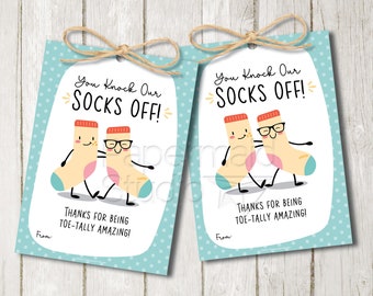 May include: Two printable gift tags with a blue background and white polka dots. The tags feature a cartoon illustration of two socks with faces and the text "You Knock Our Socks Off!" and "Thanks for being Toe-tally Amazing!"