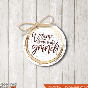 Puede incluir: Etiqueta de regalo redonda imprimible con un diseño de mancha de café. La etiqueta presenta el texto "Welcome back to the grind!" en letras marrones sobre un fondo blanco con líneas azules.
