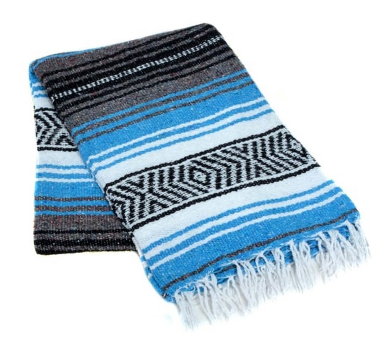 May include: A blue and white striped Mexican blanket with black accents and fringe. The blanket is folded in half and has a traditional design.