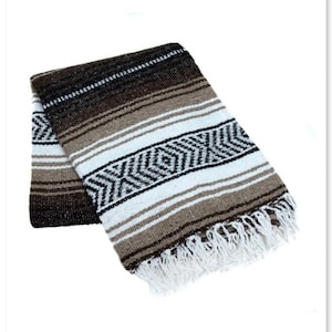 May include: A brown, white, and black striped Mexican blanket with fringe. The blanket is folded in half and has a woven pattern.