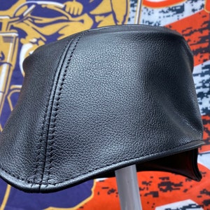 May include: A black leather motorcycle cap with a curved brim and stitched seams. The cap is designed to fit snugly and protect the head. The cap is likely made of genuine leather.