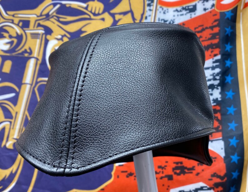 May include: A black leather motorcycle cap with a curved brim and stitched seams. The cap is designed to fit snugly and protect the head. The cap is likely made of genuine leather.