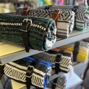 May include: A shelf display of rolled blankets with black leather straps. The blankets are in various colors and patterns, including green, black, white, and yellow.