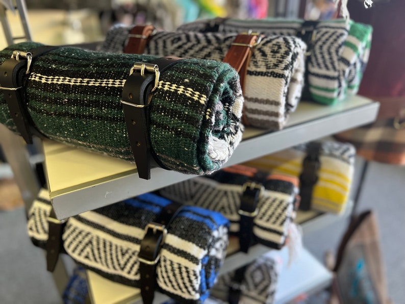 May include: A shelf display of rolled blankets with black leather straps. The blankets are in various colors and patterns, including green, black, white, and yellow.
