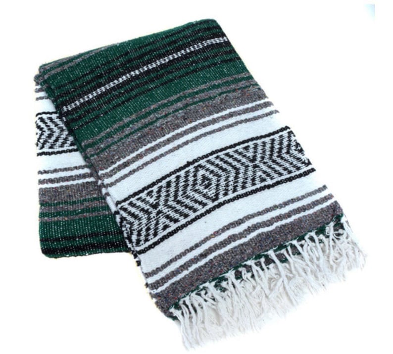 May include: A green, white, and black striped Mexican blanket with fringe. The blanket is folded in half and has a traditional pattern.