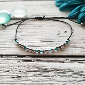 Peut inclure: Un bracelet simple en cordon noir avec des perles argentées et turquoise. Le bracelet est réglable et peut être porté au poignet ou à la cheville.