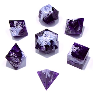 Puede incluir: Juego de siete dados poliédricos de varias formas. Los dados son de color púrpura intenso con vetas blancas y plateadas. Los dados están dispuestos sobre una superficie blanca.