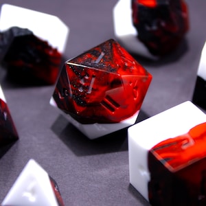 May include: A collection of polyhedral dice with a striking red and black marbled design, contrasted by white accents. The dice are arranged on a dark surface, showcasing their geometric shapes and intricate details, perfect for tabletop gaming.