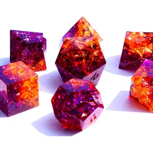 May include: Set of seven iridescent dice with a purple and orange color scheme. The dice are made of resin and have a glittery finish.