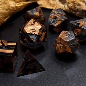 May include: A set of polyhedral dice in various shapes, including a cube, pyramid, and multi-sided dice. The dice are a mix of black and brown, with a wood-grain effect. The dice are designed for tabletop gaming.