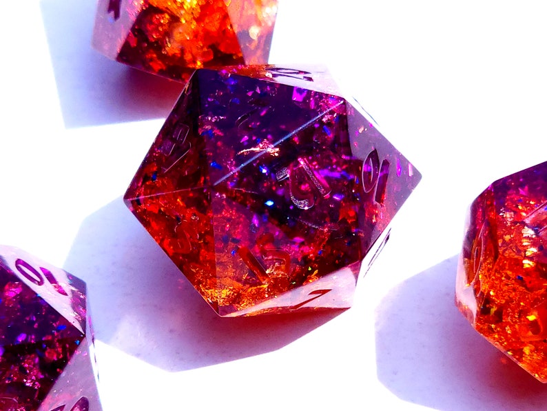 May include: Close-up of four iridescent dice with a purple and orange glitter effect. The dice are made of resin and have a clear, glossy finish.