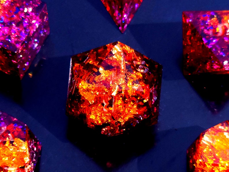 May include: A set of six iridescent dice with a variety of colors, including purple, red, and orange. The dice are made of resin and have a glittery finish.