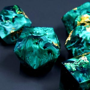May include: A set of six green and gold dice with a marbled effect. The dice are made of resin and have a unique, swirling pattern.