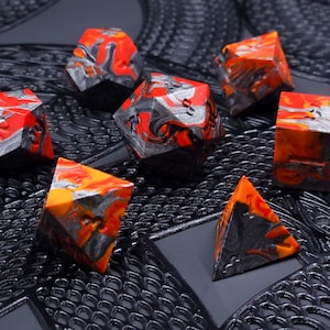 Puede incluir: Un conjunto de dados poliédricos de diversas formas, con un diseño veteado en rojo, naranja, gris y negro. Los dados están dispuestos sobre una superficie negra texturizada, mostrando sus formas geométricas.
