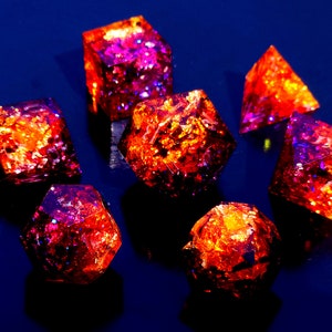 May include: A set of seven iridescent dice with a red and purple glitter finish. The dice are made of resin and have a variety of shapes, including a cube, a pyramid, and a dodecahedron.