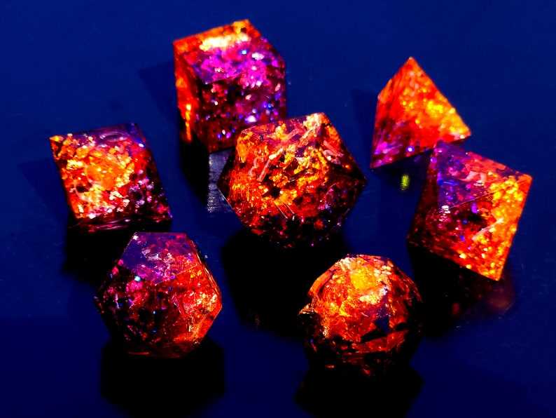May include: A set of seven iridescent dice with a red and purple glitter finish. The dice are made of resin and have a variety of shapes, including a cube, a pyramid, and a dodecahedron.
