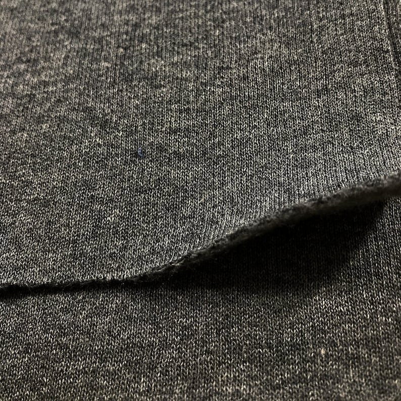May include: Close-up of a gray knit fabric with a visible seam. The fabric has a soft, textured appearance.