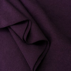May include: Close-up of a deep purple ribbed fabric folded in a soft, textured pattern.