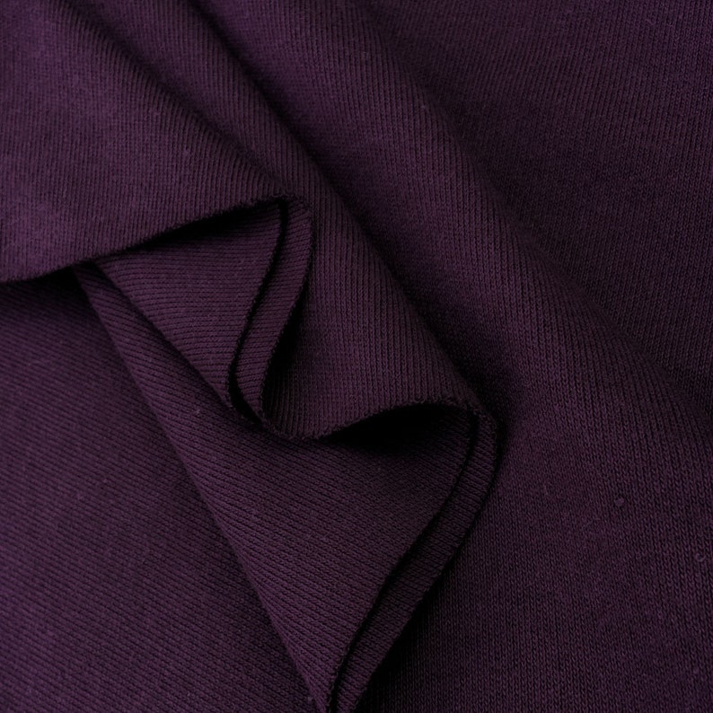 Puede incluir: Primer plano de una tela de canal&eacute; de color morado oscuro doblada en un patr&oacute;n suave y texturizado.