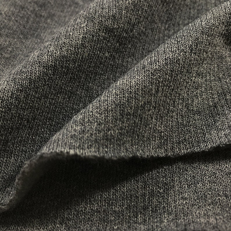 May include: Close-up of a dark gray knitted fabric with a textured surface.
