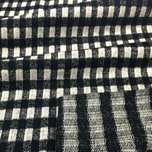 May include: Black and white checkered fabric with a textured knit pattern. The fabric is folded in a wave-like pattern.