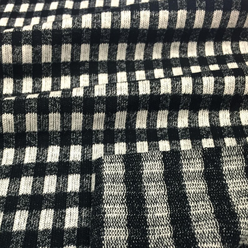 May include: Black and white checkered fabric with a textured knit pattern. The fabric is folded in a wave-like pattern.