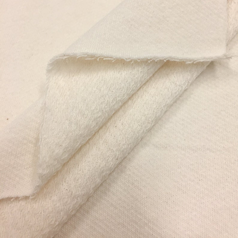 May include: Close-up of a white, soft, and textured fabric. The fabric is folded in half, showing the inside and outside of the material.