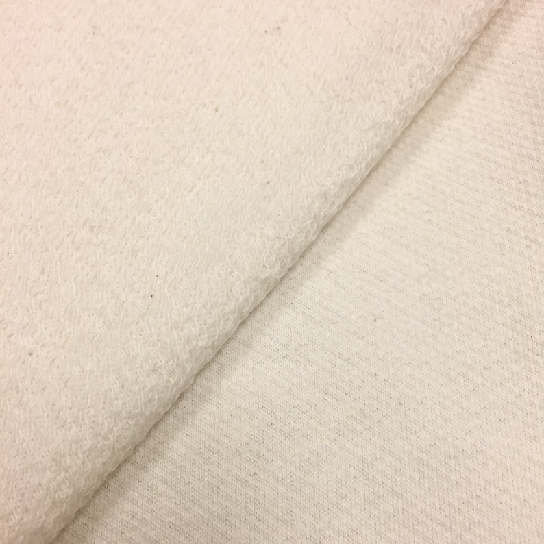 May include: Close-up of a white fabric with a soft, fuzzy texture. The fabric is folded in half, showing both sides.