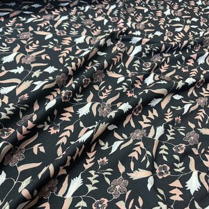 May include: Black fabric with a repeating floral pattern. The design features stylized flowers and leaves in shades of pink, white, and tan. The fabric is likely used for clothing or home decor.