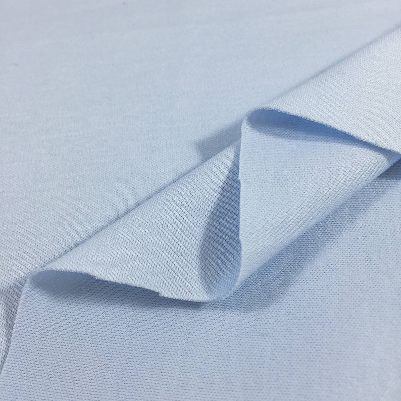 May include: A close-up of a light blue fabric with a textured surface. The fabric is folded in half, showing the inside of the fabric.