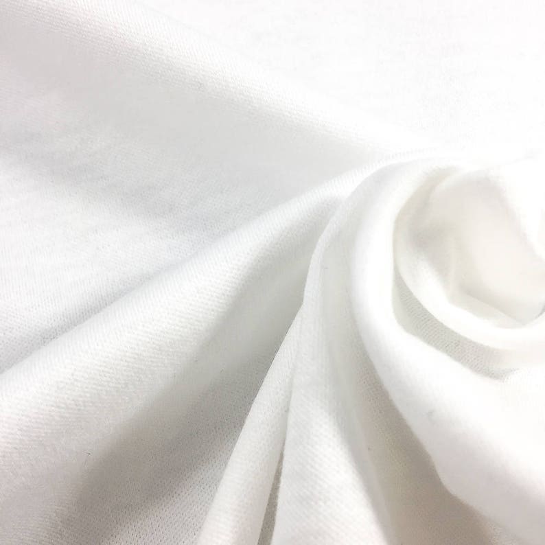 May include: White cotton fabric with a soft, smooth texture. The fabric is folded and draped, showing its natural drape and flexibility.