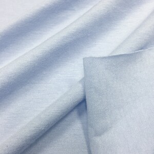 May include: A close-up of a light blue fabric with a smooth, soft texture. The fabric is folded and draped, showcasing its draping qualities.